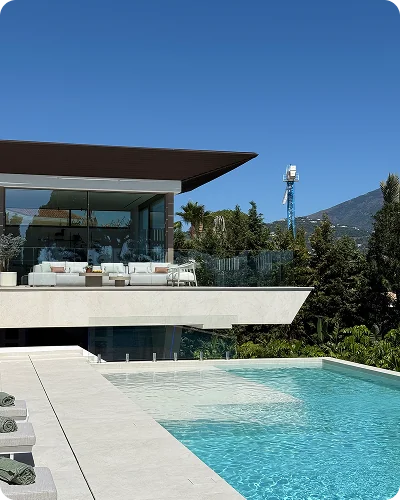 A villa terrace with outdoor sofas above a turquoise pool, with hills behind