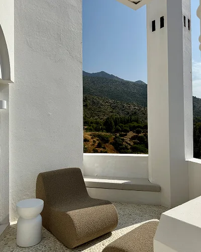 A whitewashed terrace with a lounge chair, looking out over green hills